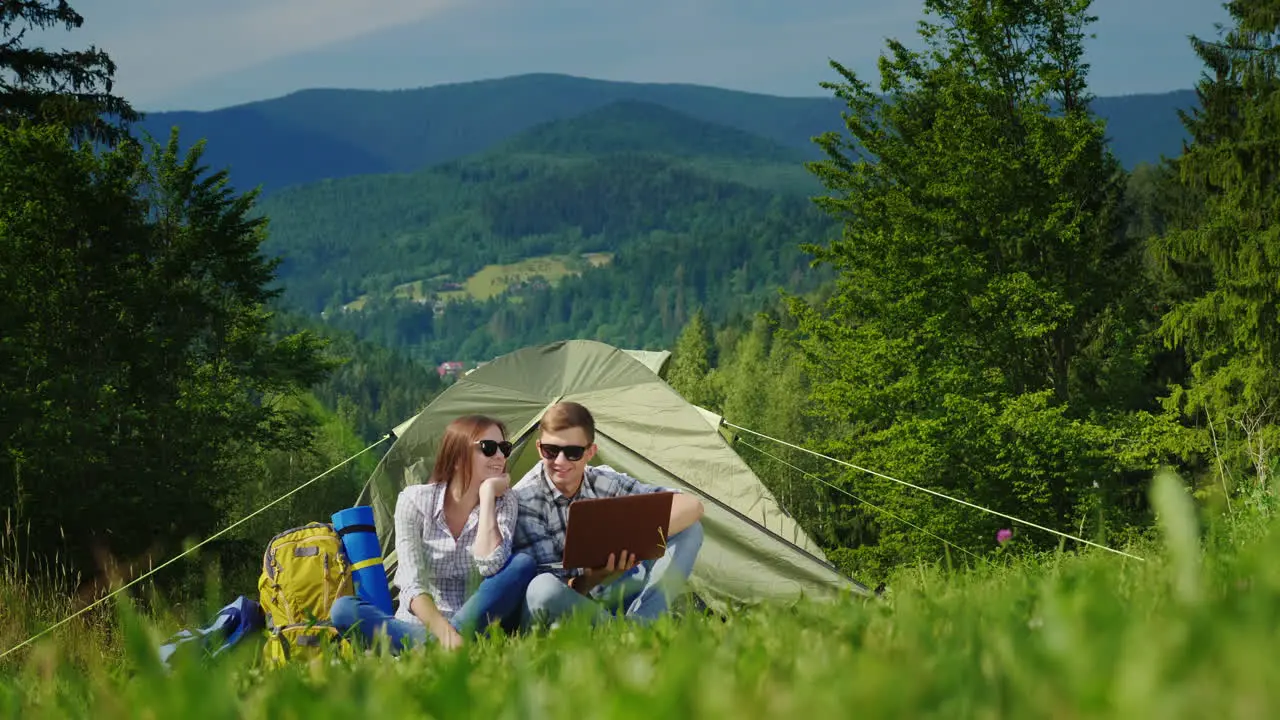 A Young Couple Is Using A Laptop While Camping With A Tent 1