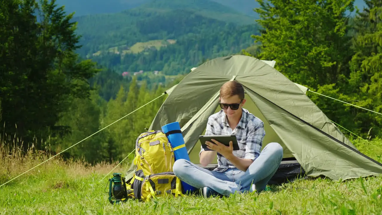 A Young Male Tourist Uses A Laptop While Camping Near A Tent