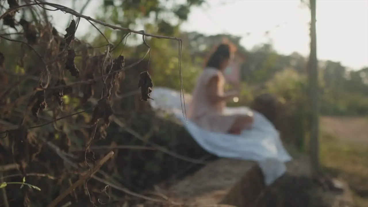 Static slow motion close up shot of withered plants with dry leaves in the background a young woman sitting on a white sheet on the stairs