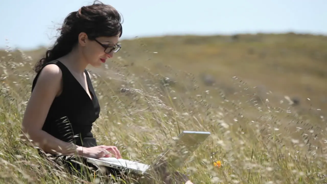 A woman using a laptop sits in a field 2