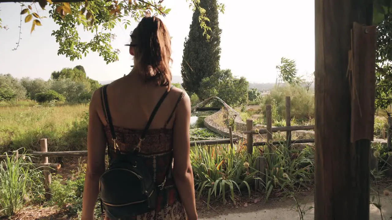 Woman discovers the garden and pond of perfumery museum in summer back rear view