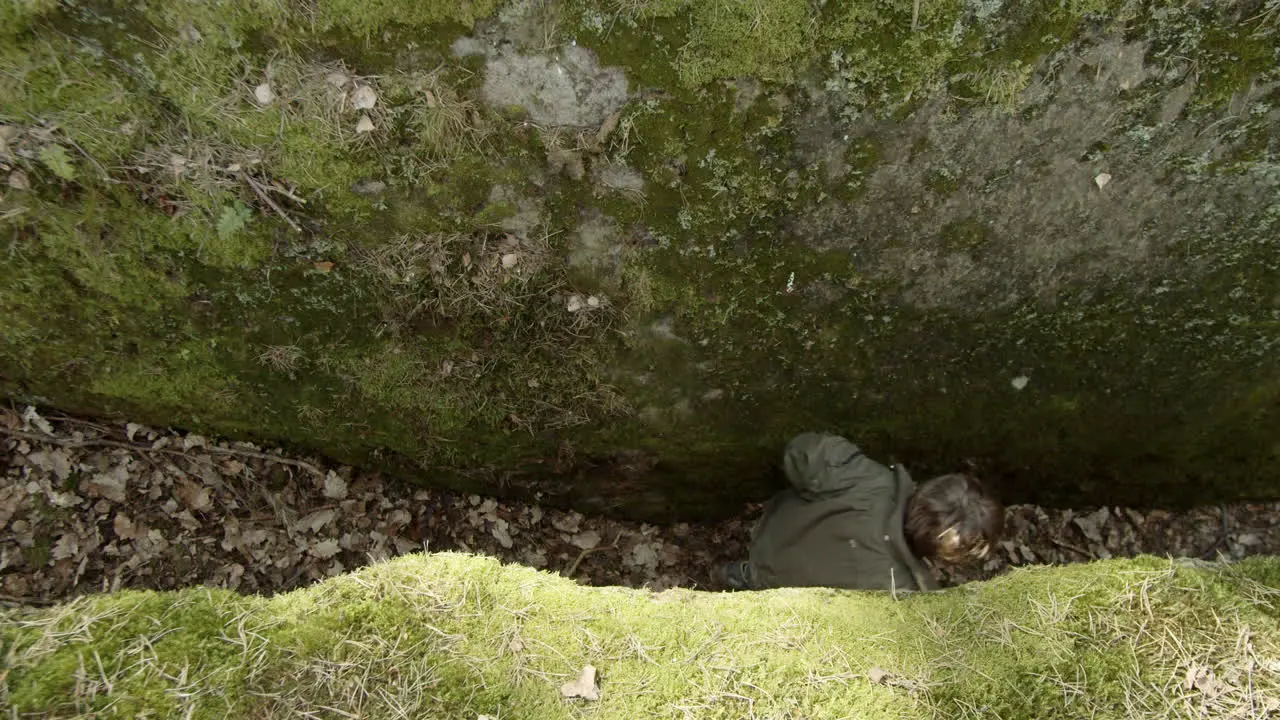 Young boy passing in between two giant boulders adventuring through forest Overhead wide static shot