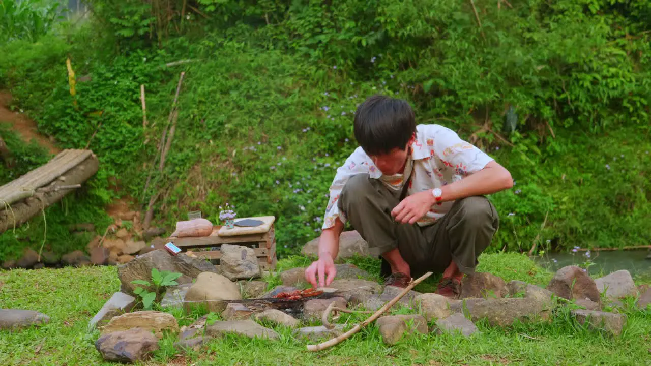 Asian young man eating on rural green ground making rustic barbecue