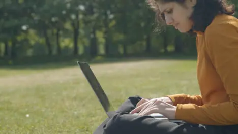 Handheld Shot of Student Working and Typing On Laptop In a Park