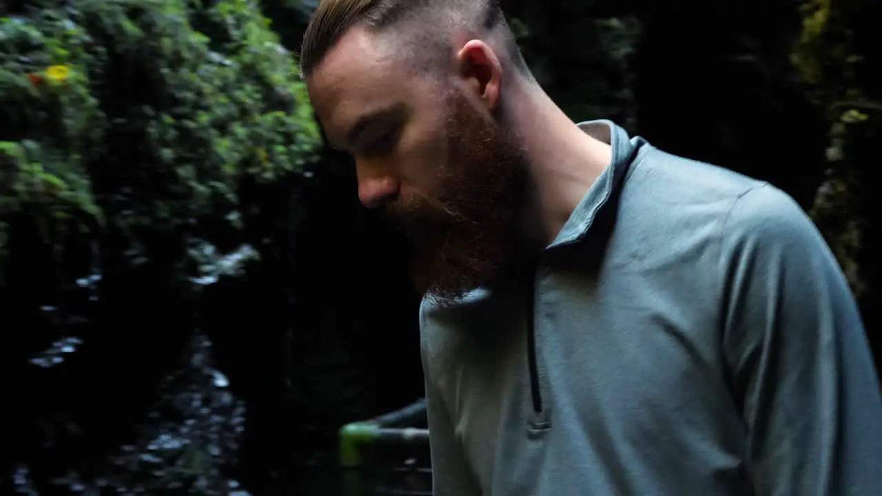 Young man slowly walking in cave-like place and looking down with water trickling