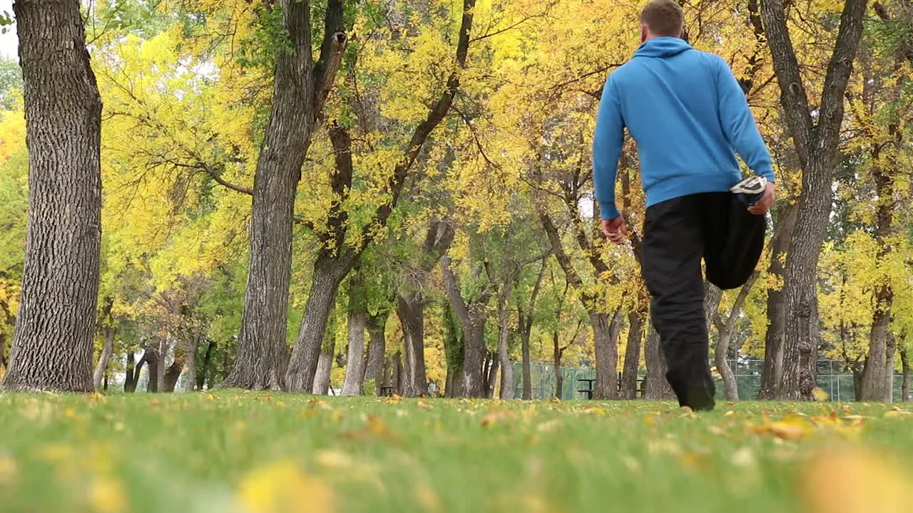 An Active Man Doing Fitness Exercises In The Park With Tall Trees And Lush Grass On An Early Morning ground-level shot