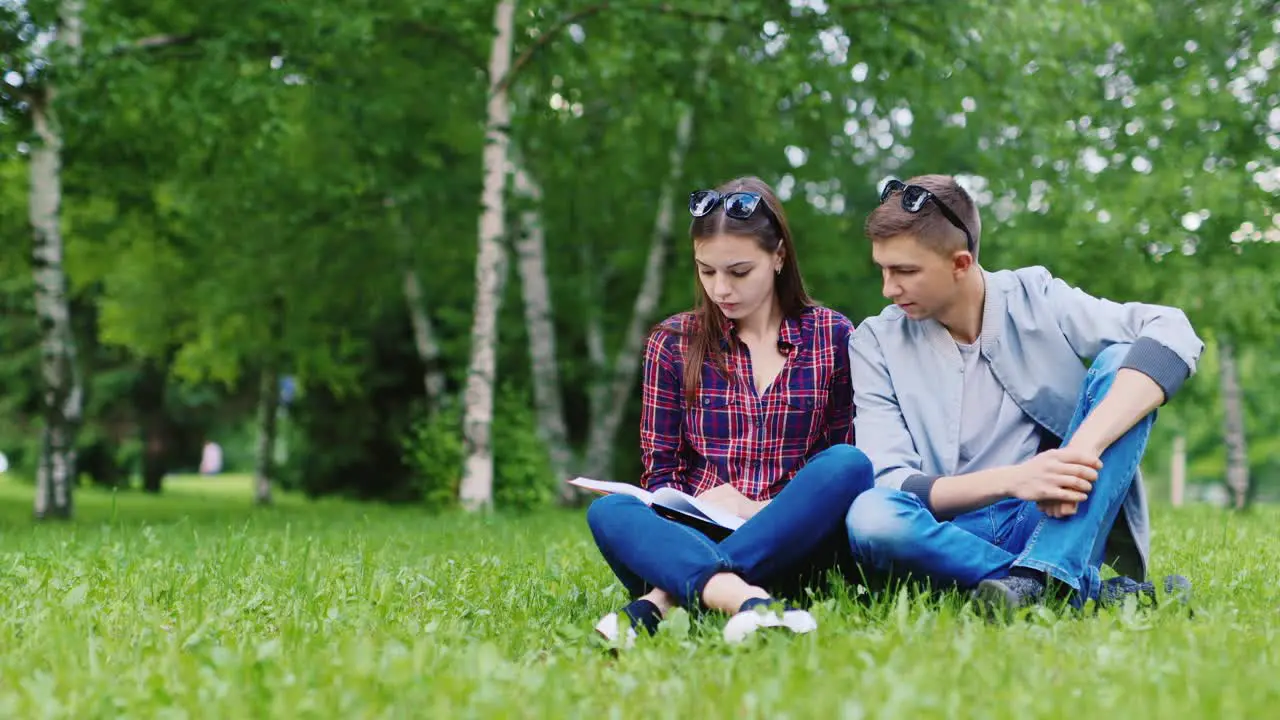 Young Man And Woman Sitting On Grass Looking at Book