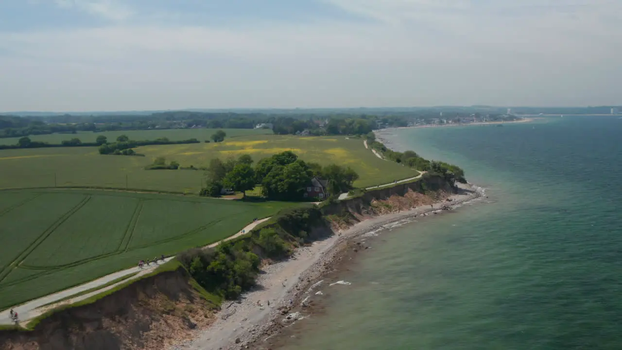 Circle pan aerial drone view of shoreline beach with vast green field in Brodten Germany on peaceful spring day