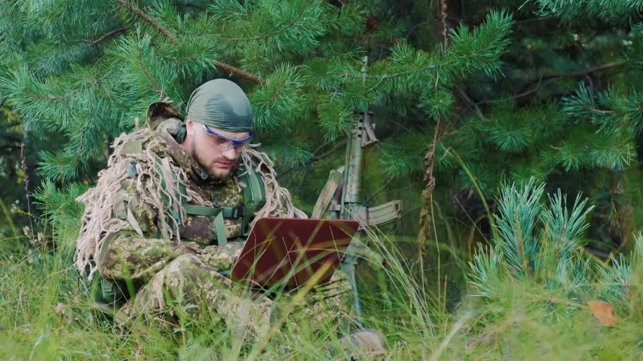 Armed Men In Camouflage Sitting In The Bush Uses A Laptop