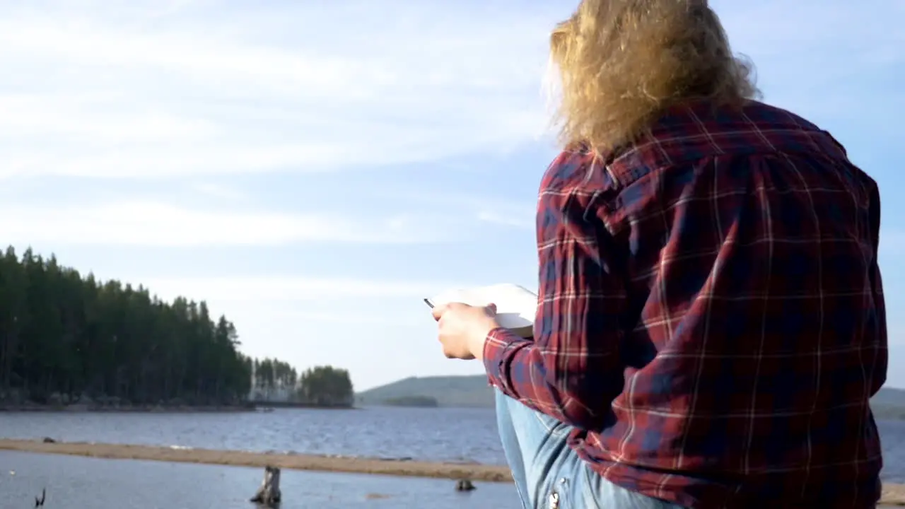 Girl sitting and reading a book at a lake on a sunny day