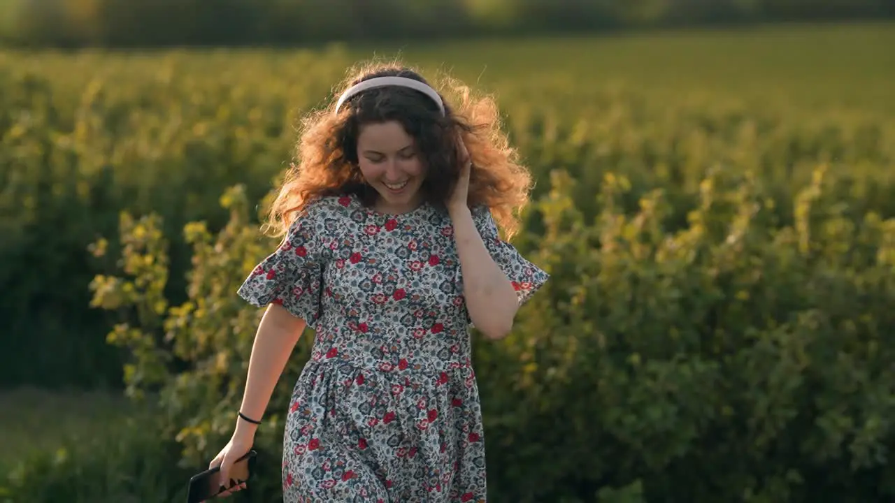 Portrait of red-haired woman listening to music in headphones on nature and dancing