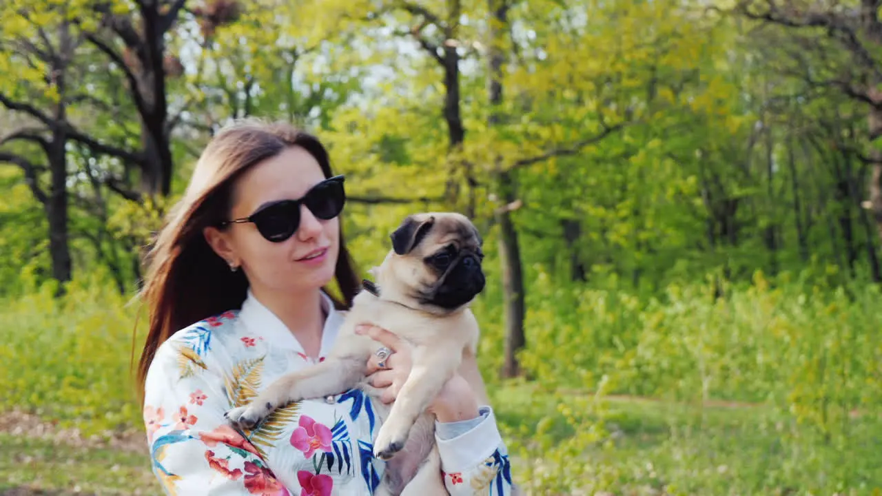 Young Stylish Woman In Sunglasses Walking In The Park With A Dog Of Pug Breed