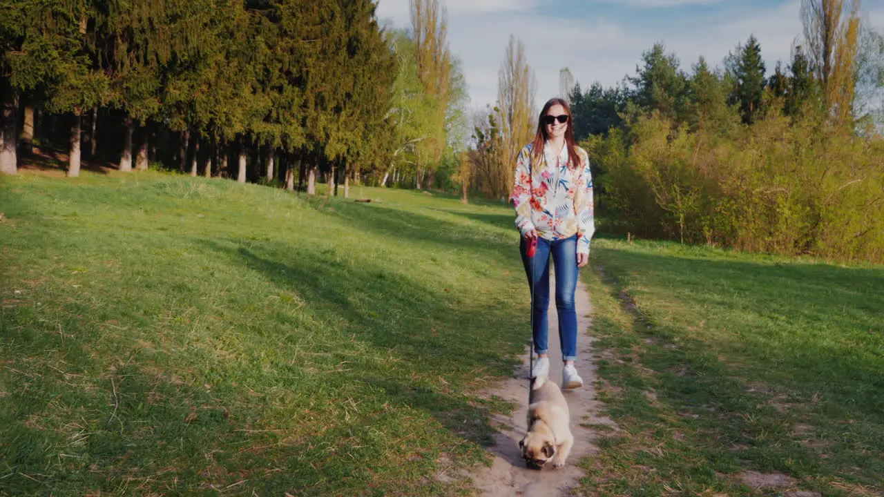 Young Stylish Woman In Sunglasses Walking In The Park With A Dog Of Pug Breed 1