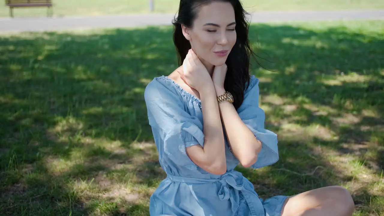 Portrait of attractive brunette woman in blue dress sitting in a park