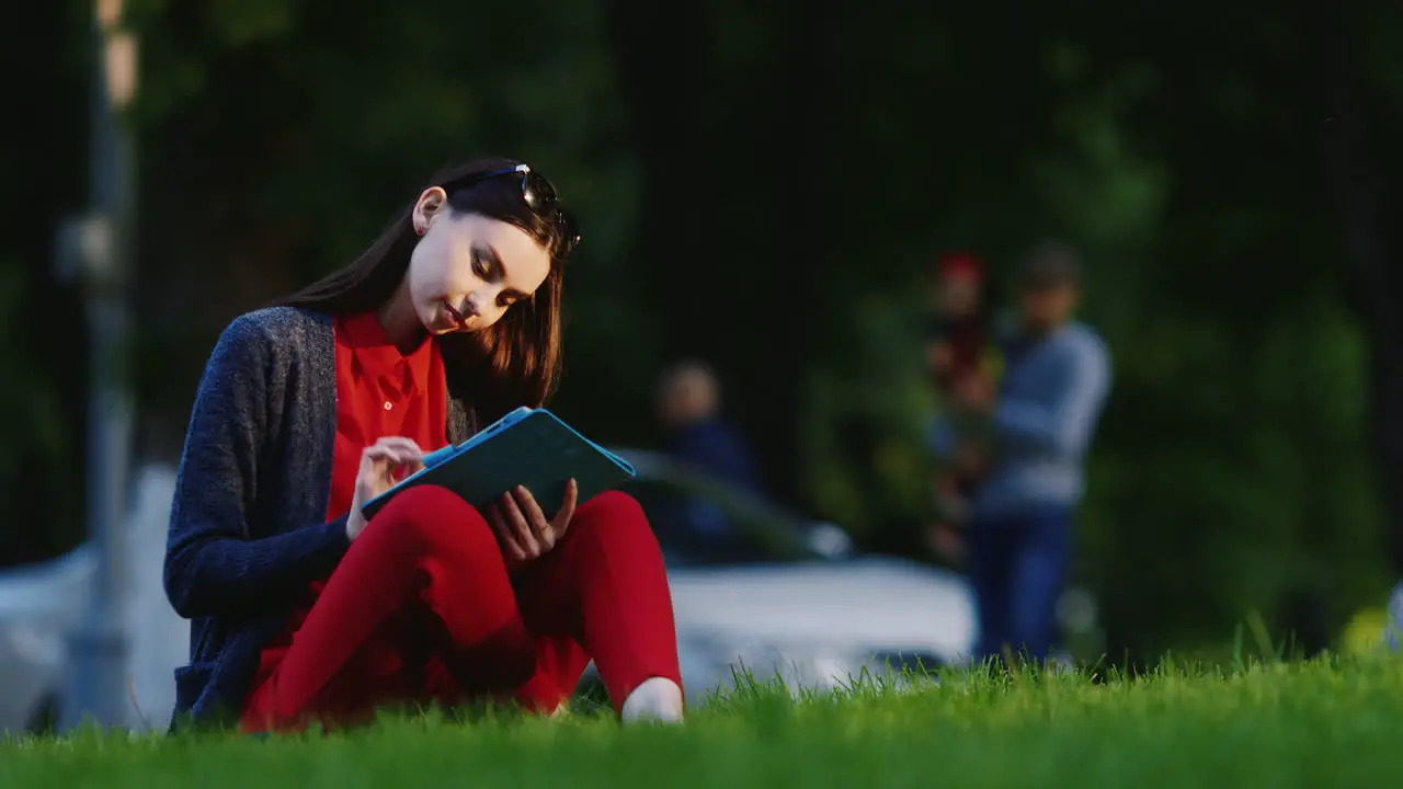 Stylish Woman Sitting On The Grass In The Park Enjoying The Tablet In The Background People Walk Hd 