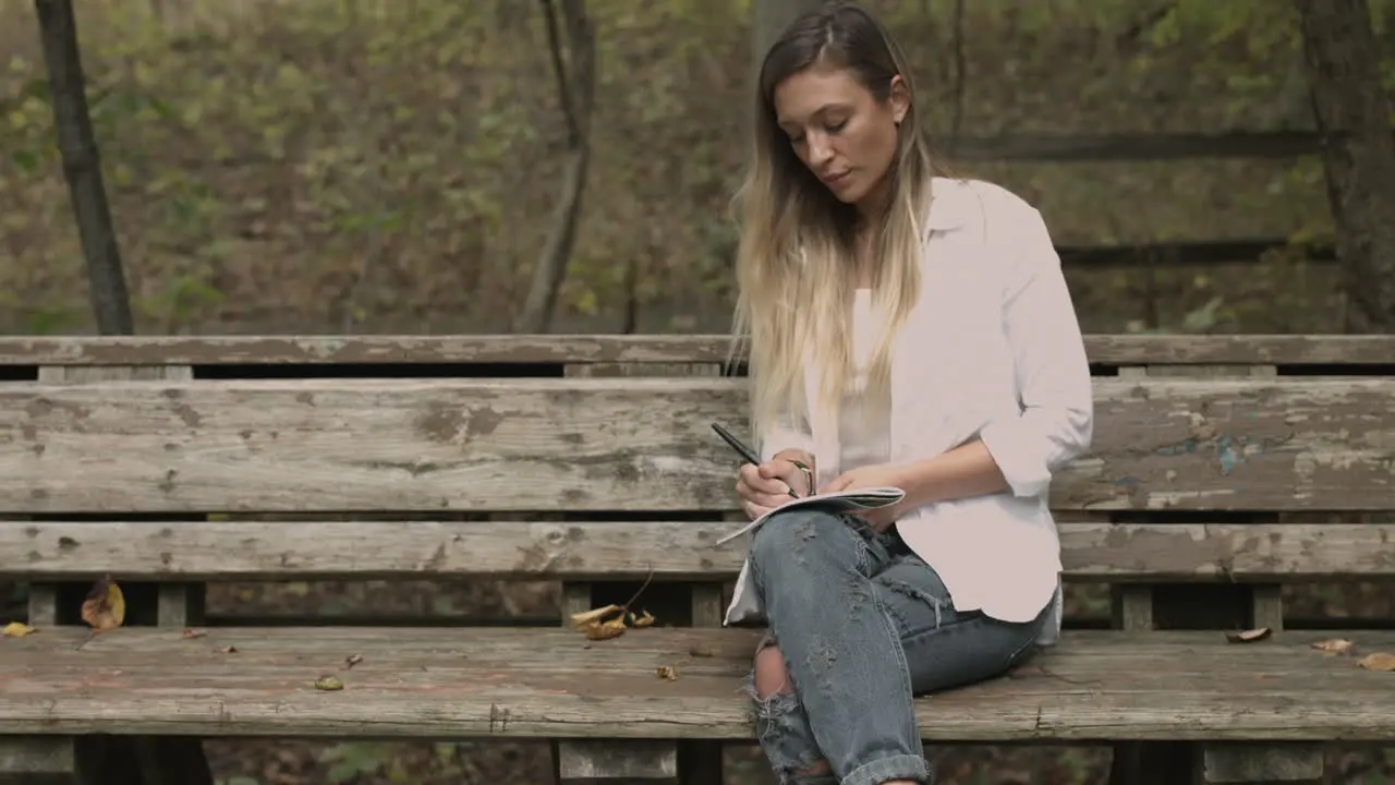 Young female sits in a forest park with a sketch pad slider dolly shot