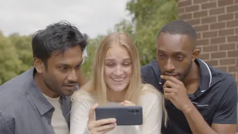 Multi-Cultural Friends Celebrating Watching Sports Game On Mobile Phone Outdoors Together