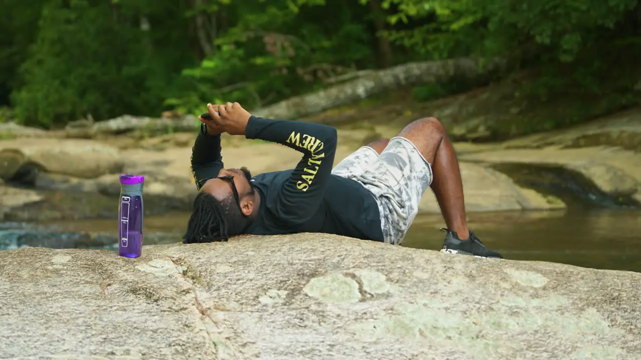 A man lays down on a giant rock in the middle of a lush green forest