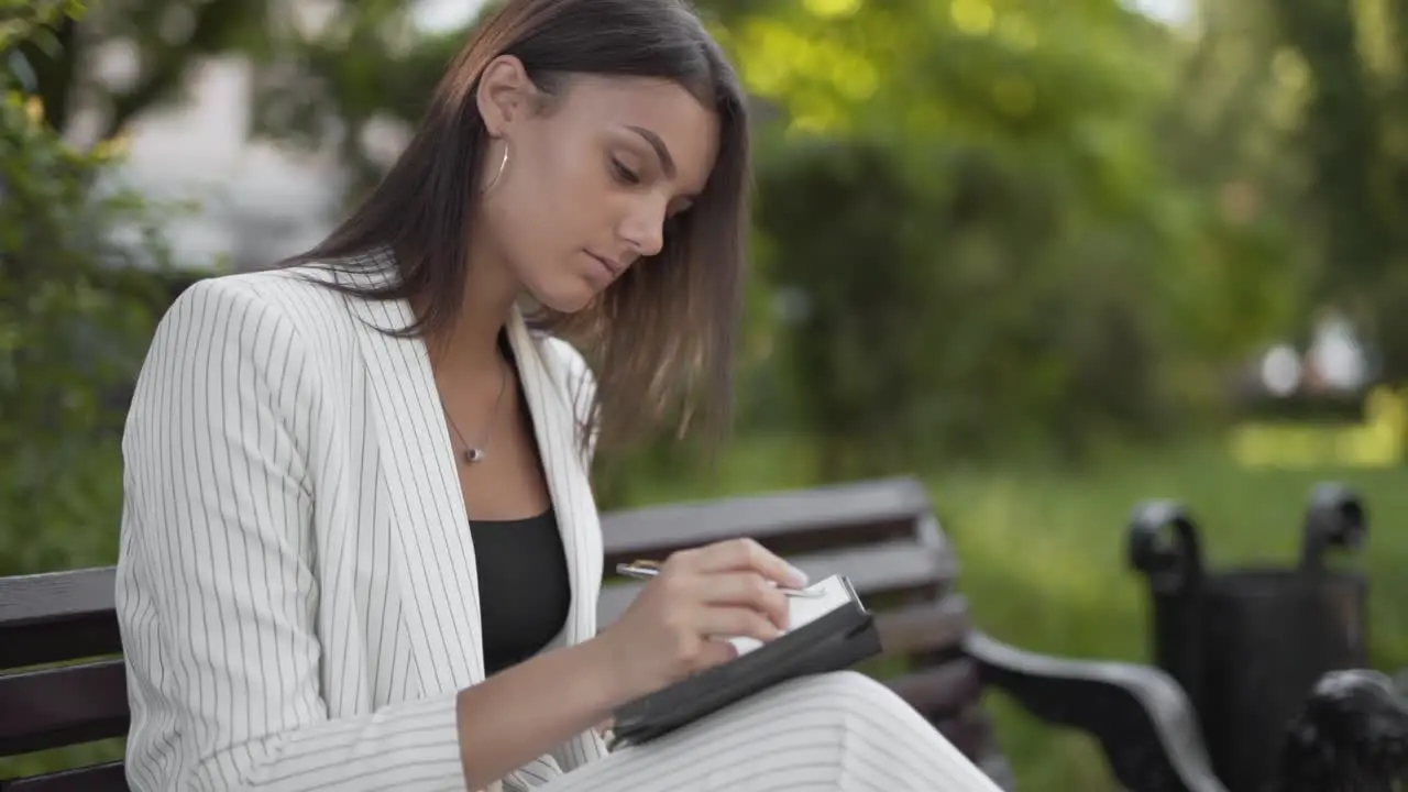 Busy businesswoman writing down ideas on a notepad on a bench