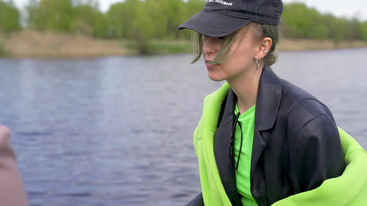 Young Woman With Black Cap And Leather Jacket Holding Camera Next To Beer Bottles On The Riverside