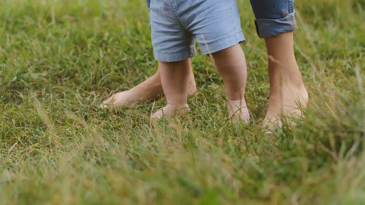 Close Up Of The Bare Feet Of Baby And Mother Taking First Steps On The Green Grass