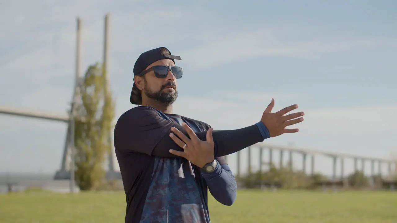 Handsome Sportsman In Sunglasses Warming Up And Stretching Arm Outdoors