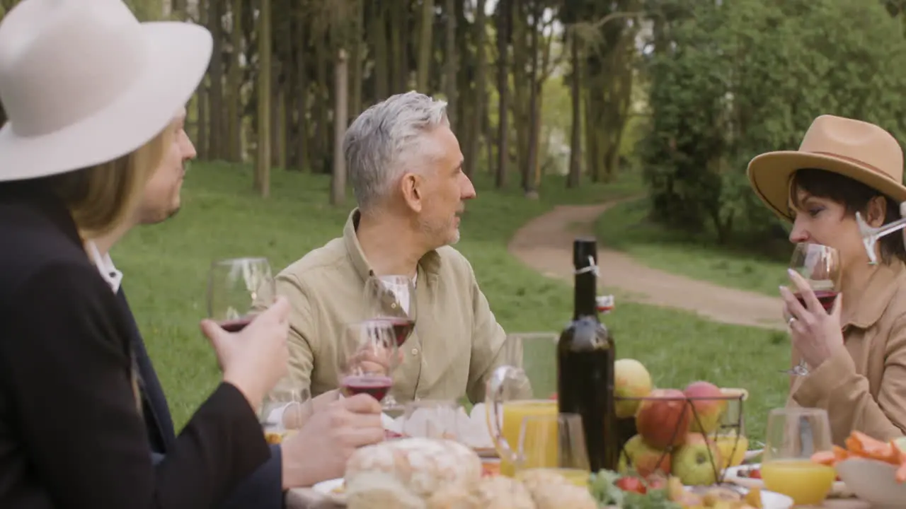 Group Of Happy Friends Talking Together While Sitting At Table During An Outdoor Party In The Park