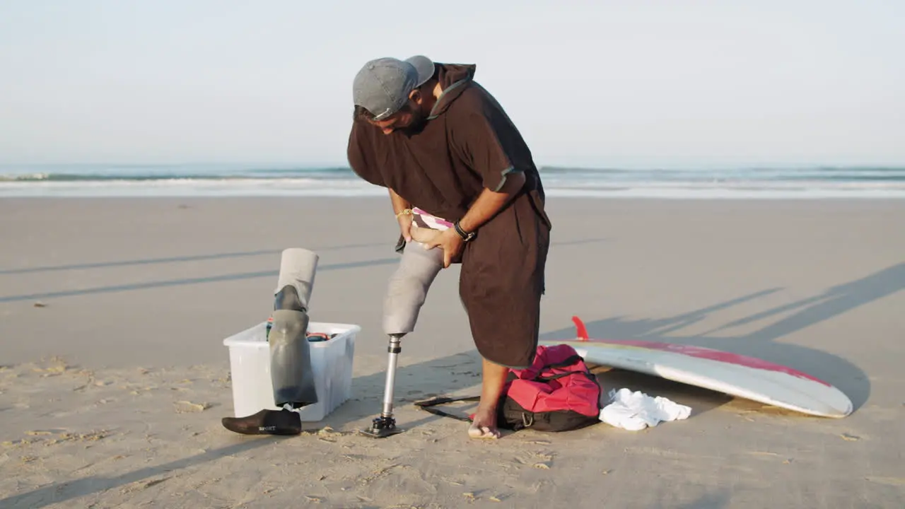 Long Shot Of A Male Surfer On The Beach Putting Prosthetic Leg On