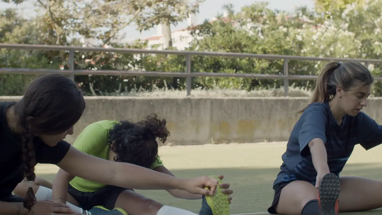 Female Football Players Sitting On The Field And Stretching Legs