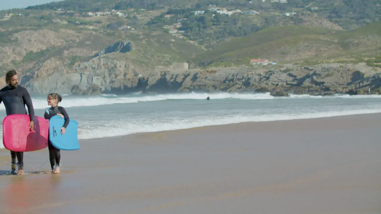 Surfer With Artificial Leg And Daughter Holding Surfboard And Talking While Walking On The Beach