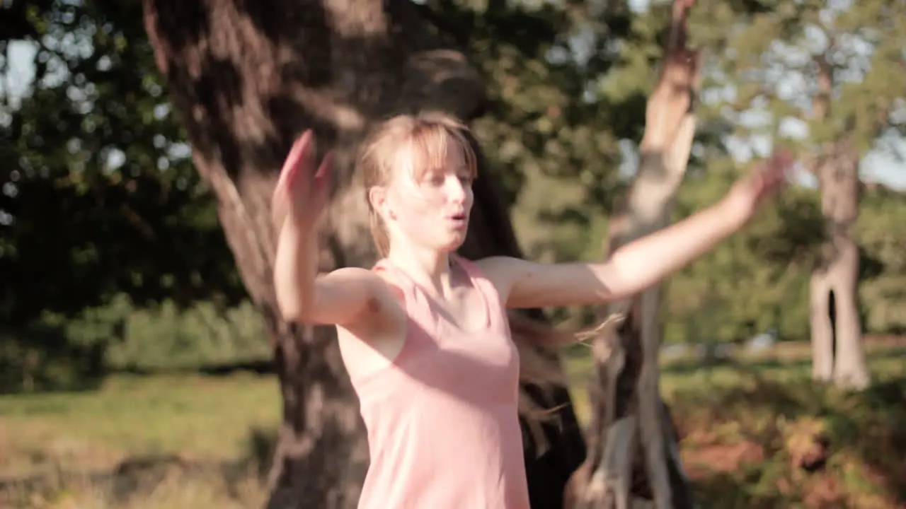 On a sunny day in the park a young woman doing jumping jacks in front of the tree