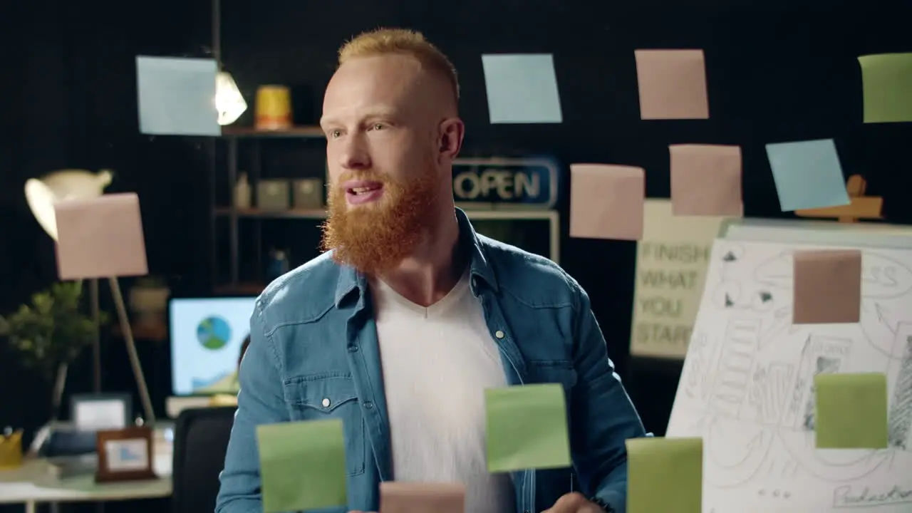 Closeup smiling hipster guy sticking notes on glass board on night office