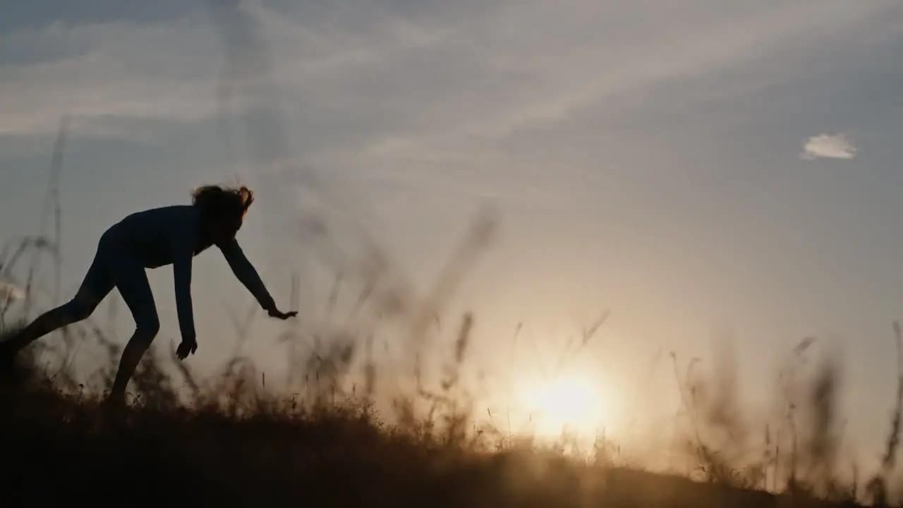 Child does acrobatic exercises in meadow at sunset