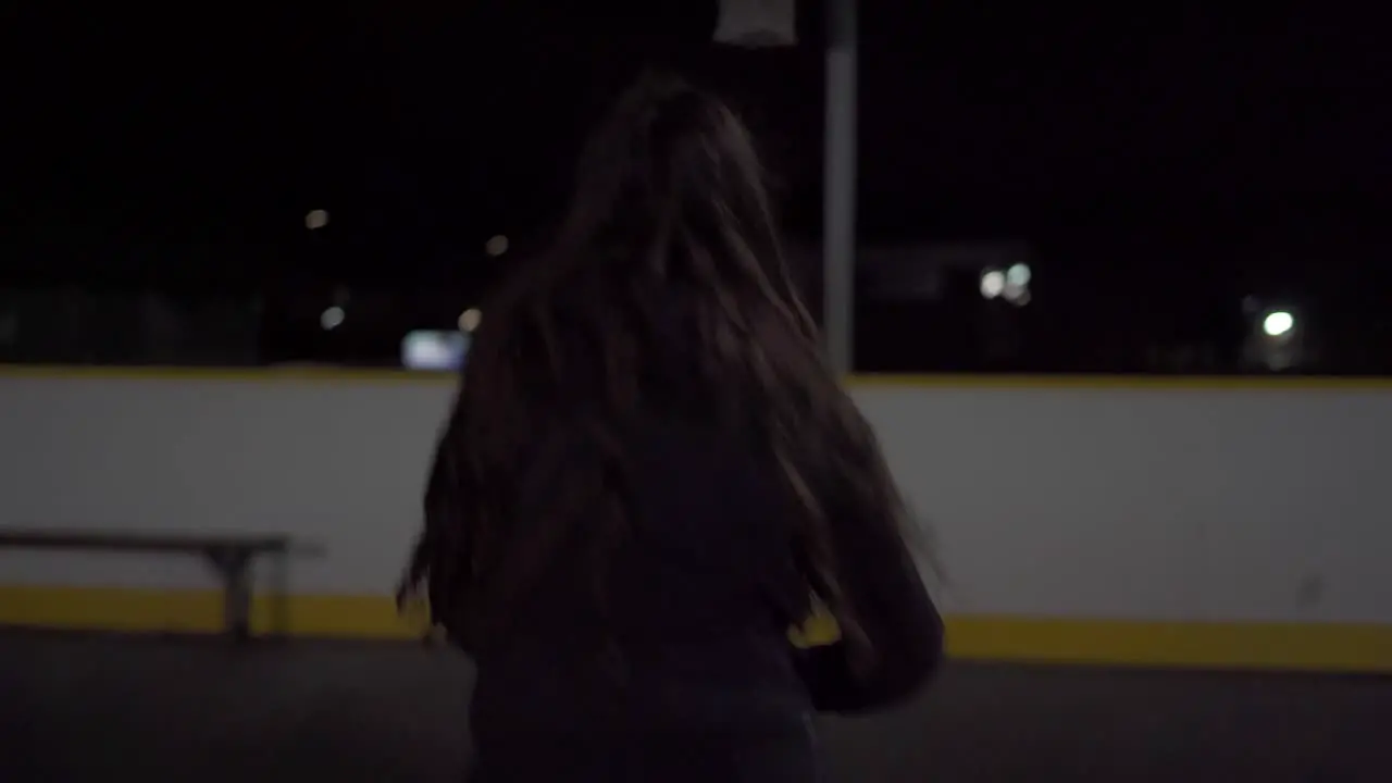 Dynamic push in shot of teenage girl shooting basketball and getting swish at outdoor court at night