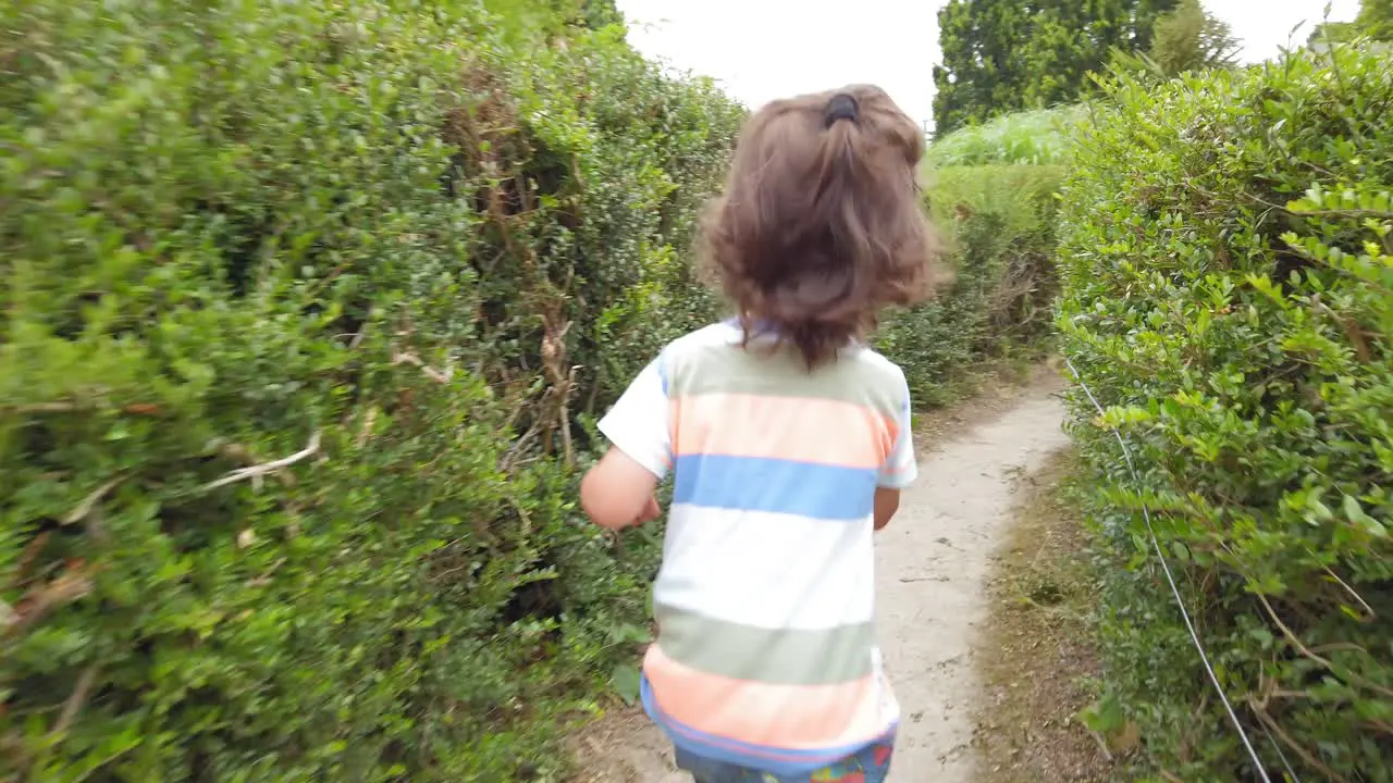 Baby boy with long hair running through a hedge maze in slow motion