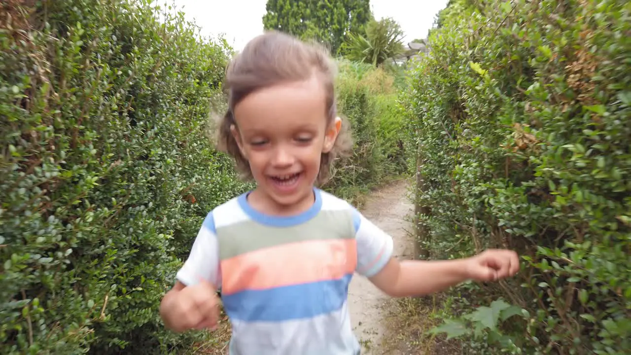 Baby boy with long hair running through a hedge maze in slow motion front view