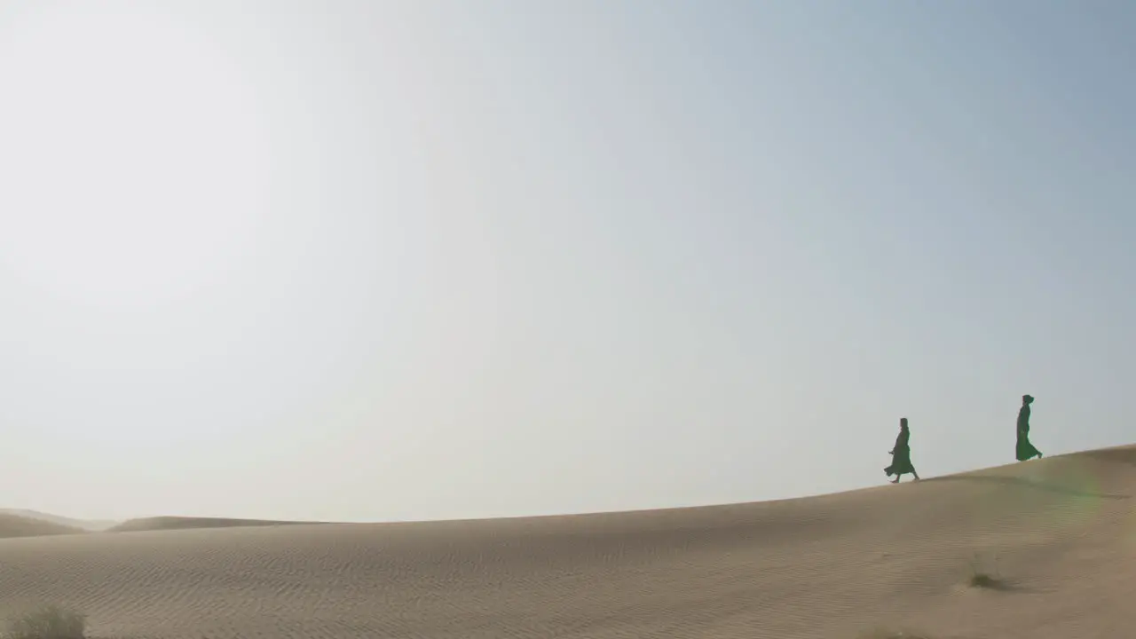 Extreme Long Shot Of Two Muslim Women Wearing Traditional Black Dress And Hijab Walking In A Windy Desert