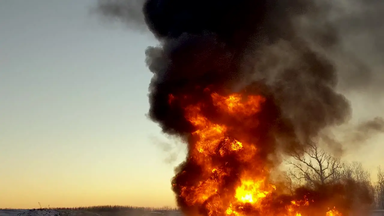 Zoom in on huge cloud of black smoke billowing into the sky as an oil spill burns up on the ground below