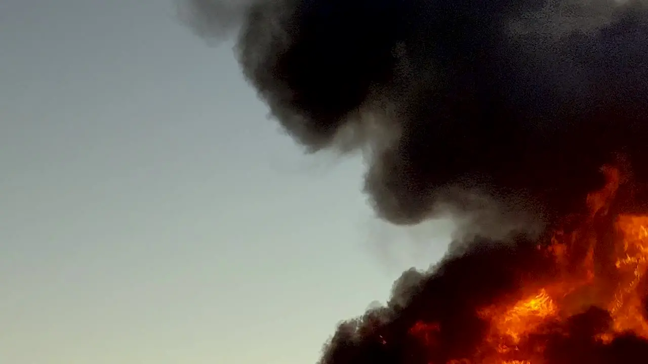 Huge dangerous raging fire burns rapidly sending thick black flames into the sky