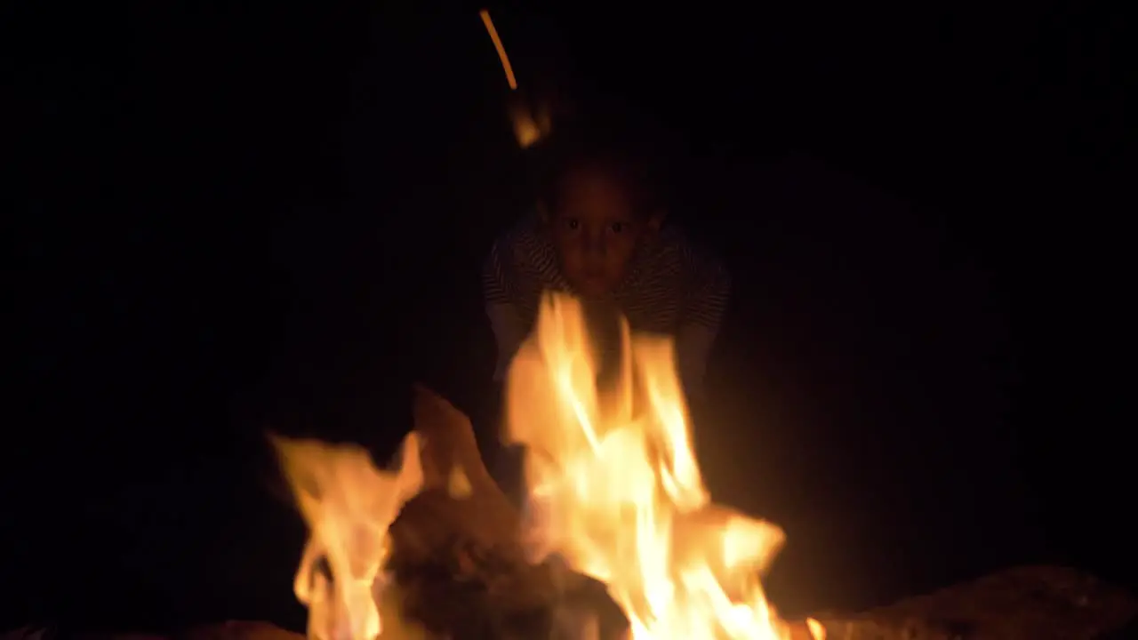 A young mixed raced child's face is lit up by the light of a camp fire at night