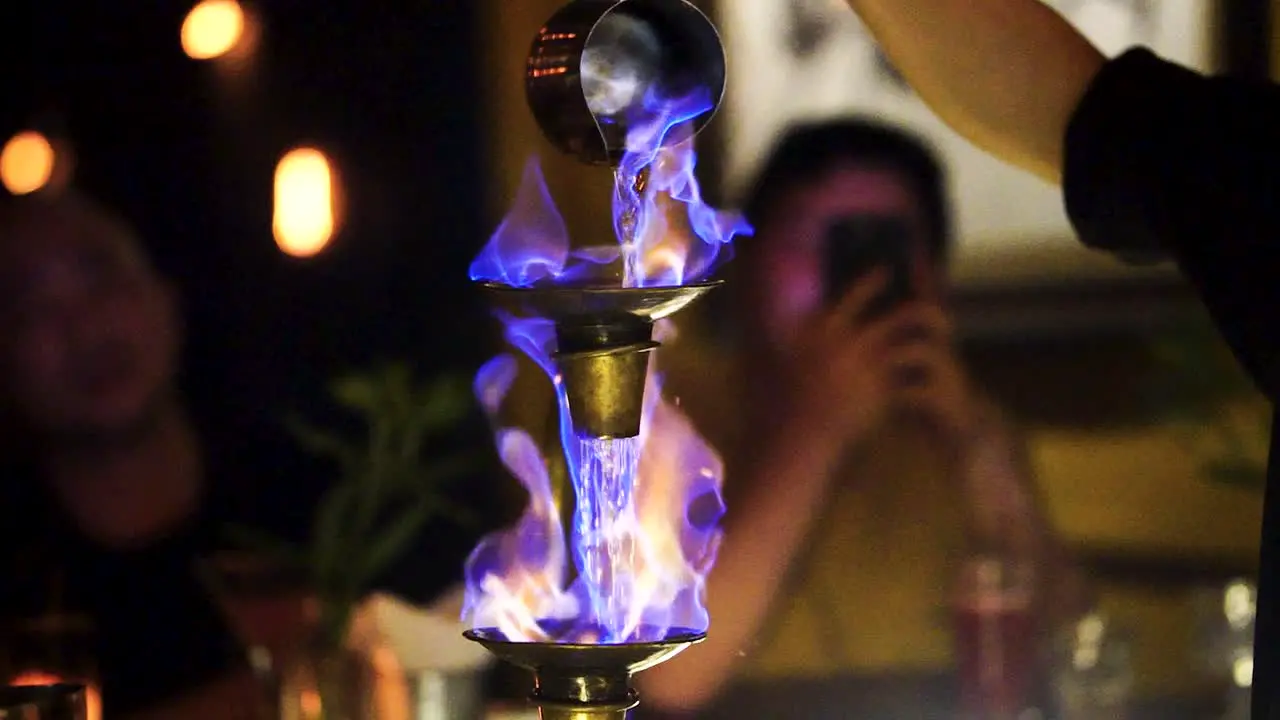 Bartender Pouring Flaming Blue Flame Cocktail Onto Tiered Cups In Hanoi