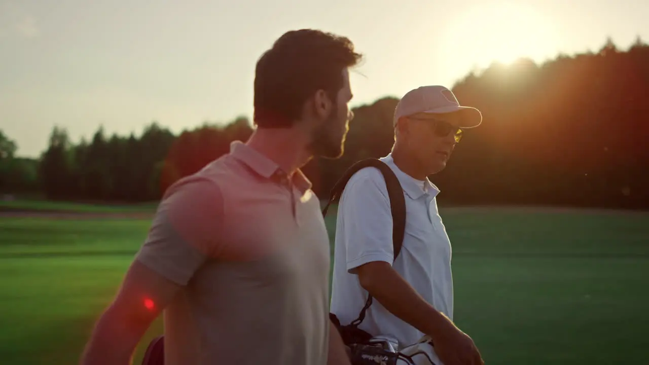 Golf players looking sunset on summer field Golfers group walk course fairway