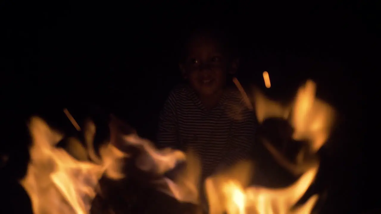 A close up of a young mixed raced child's face as he leans and looks into the flames of a camp fire