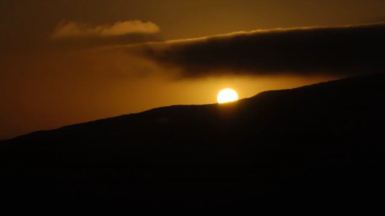 Time lapse of sun disappearing behind mountain top at sunset