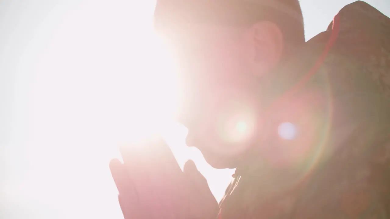 A person in a warm winter jacket warms hands steams from his mouth setting sun over snowy landscape