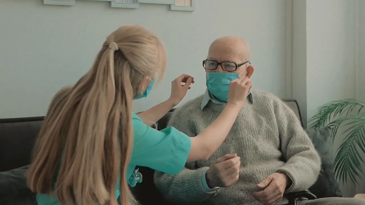 Female Caring Nurse Puts On Face Mask On Elderly Male