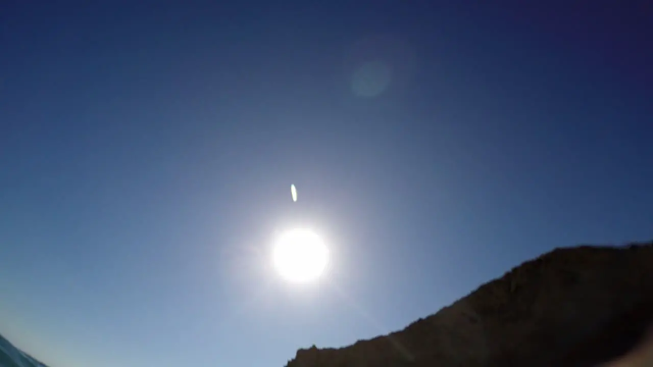 View of horizon with big sun behind cliff from water surface at sea