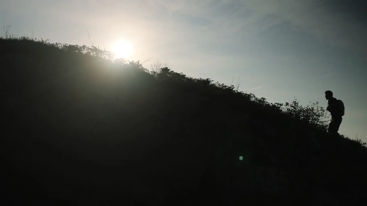 Man walking uphill with a backpack silhouette feeling with bright sun behind