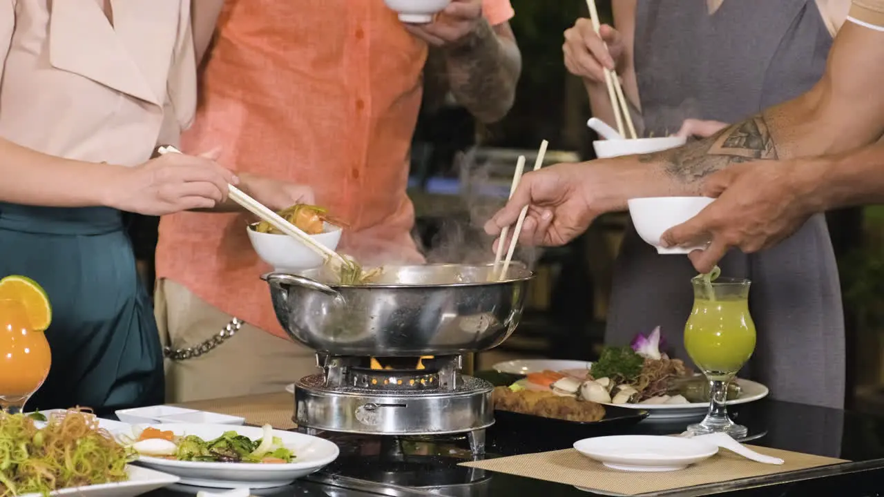 People standing and picking food from hot pot to their white bowls