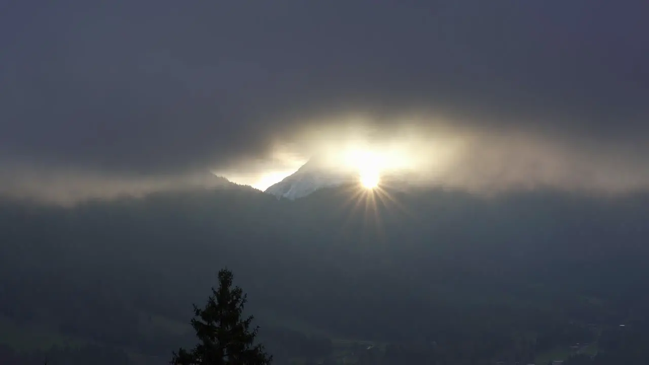 Sun star shines through the clouds at dawn between a mountain gap in the alps